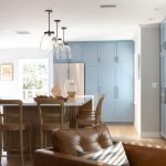 1950's Kitchen Remodel in Westchester, CA. open-concept kitchen and living area with blue cabinetry, white quartz countertops, wood island with bar seating, glass pendant lighting, brown leather furniture, and modern fixtures throughout.